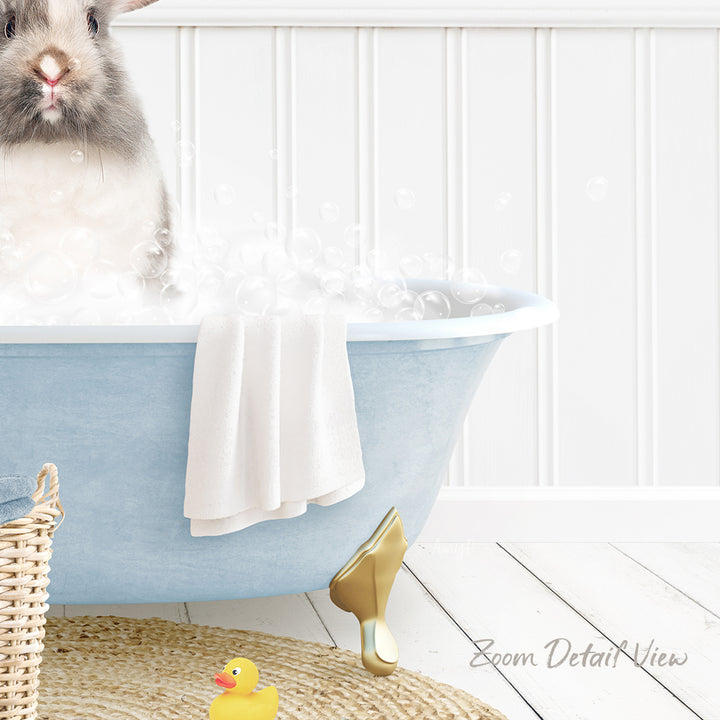A fluffy gray rabbit sitting in a blue bathtub filled with bubbles, surrounded by a yellow rubber duck and a white towel.