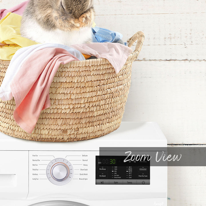 A cat sitting in a woven laundry basket filled with clothes, with a white washing machine in the background displaying a "Zoom View" interface.