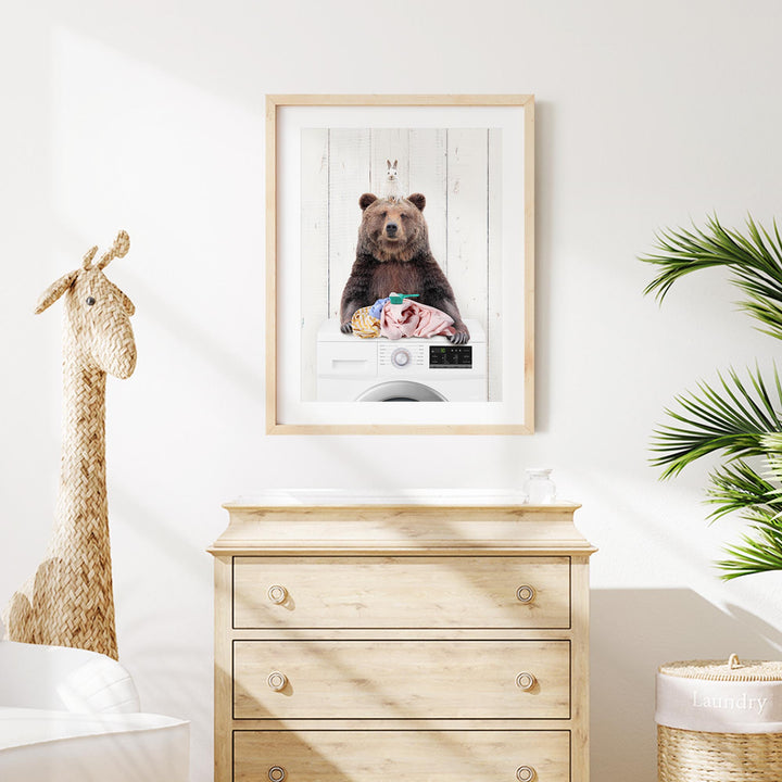 a framed photo of a bear sitting on a washing machine, surrounded by laundry.