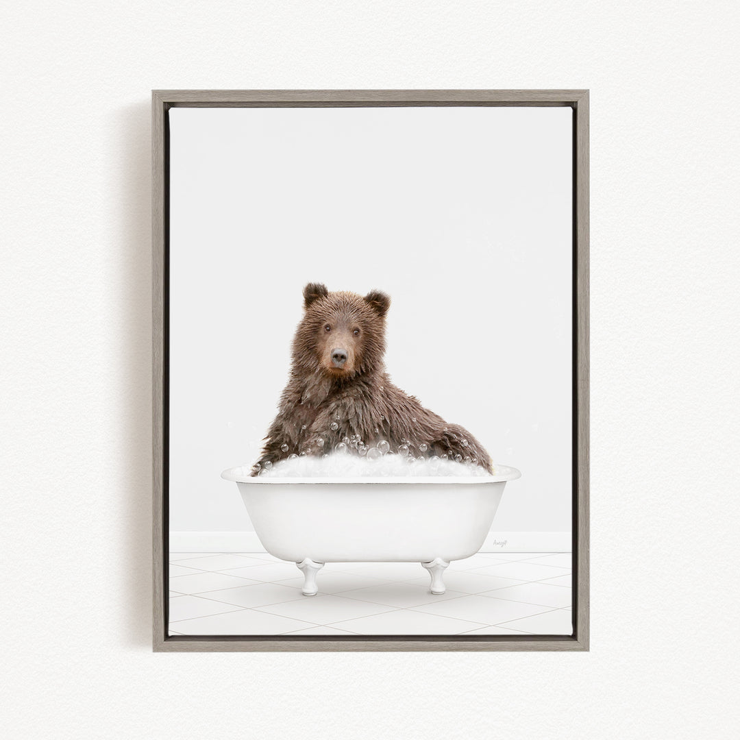 A brown bear sitting in a white bathtub filled with bubbles.
