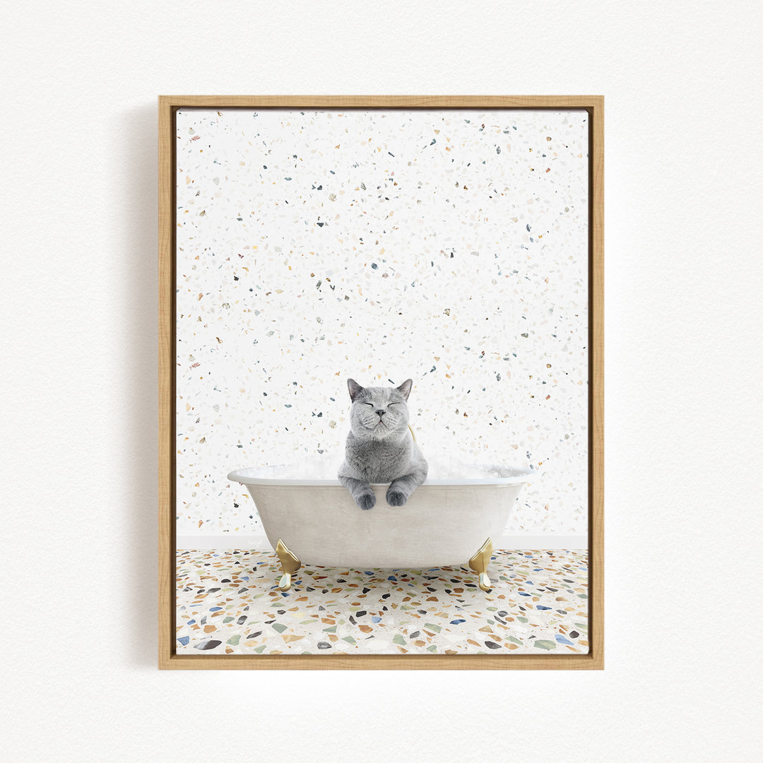 A gray cat sitting in a white bathtub filled with bubbles, surrounded by a speckled tiled floor.