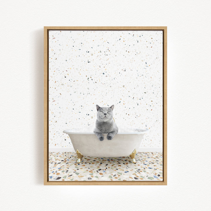A gray cat sitting in a white bathtub filled with bubbles, surrounded by a speckled tiled floor.