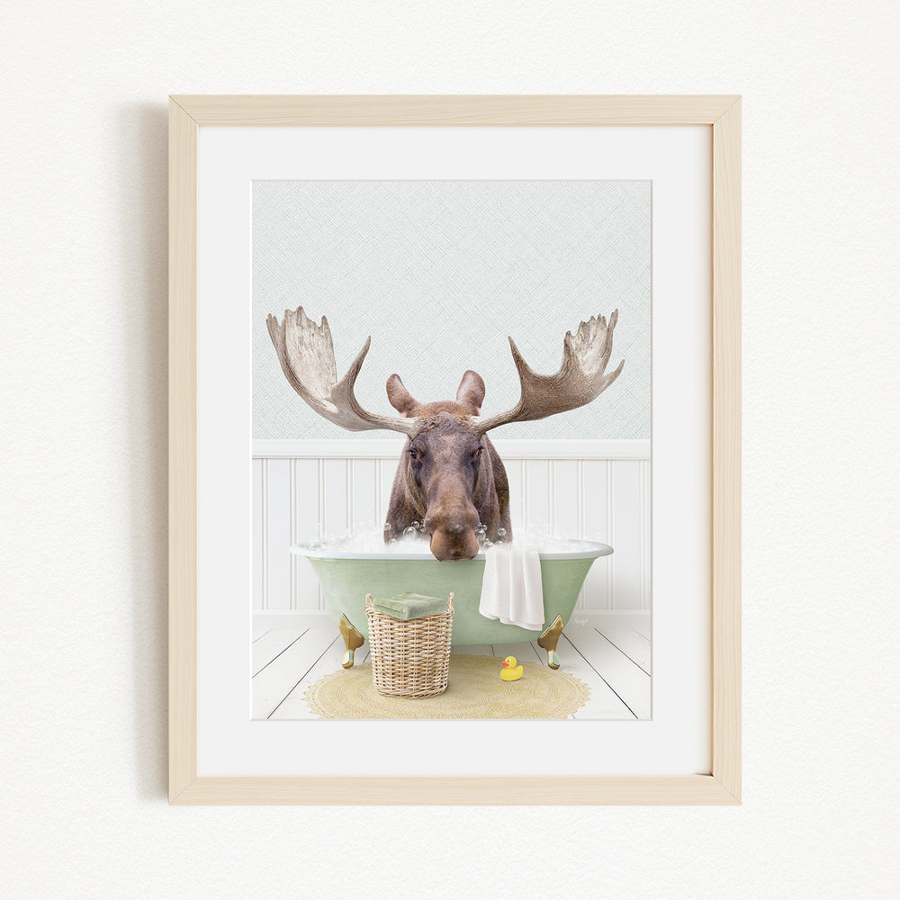 A moose with large antlers is sitting in a green bathtub, surrounded by a basket of rubber ducks and a yellow rubber ducky.