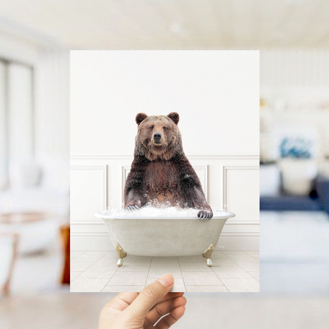 A hand holds up a framed image of a brown bear sitting in a bathtub filled with water, creating a whimsical and playful scene.