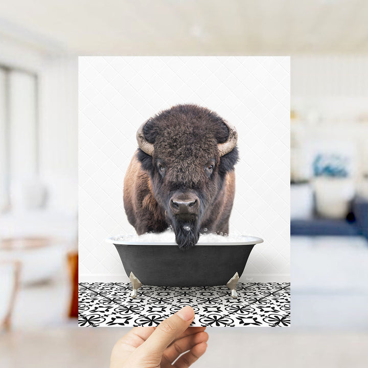 A close-up of a bison's head peeking out of a bathtub, with a hand holding the image up to the viewer.