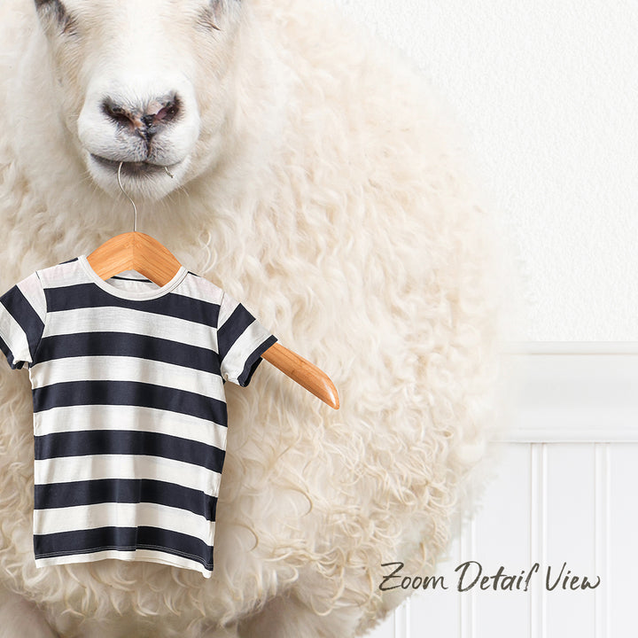 A fluffy white sheep is standing next to a wooden hanger with a striped shirt on it.
