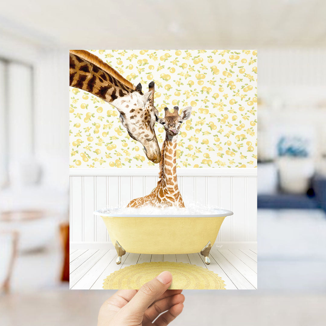 A hand holds up a framed photograph of two giraffes sitting in a yellow bathtub, surrounded by a yellow and white floral pattern.