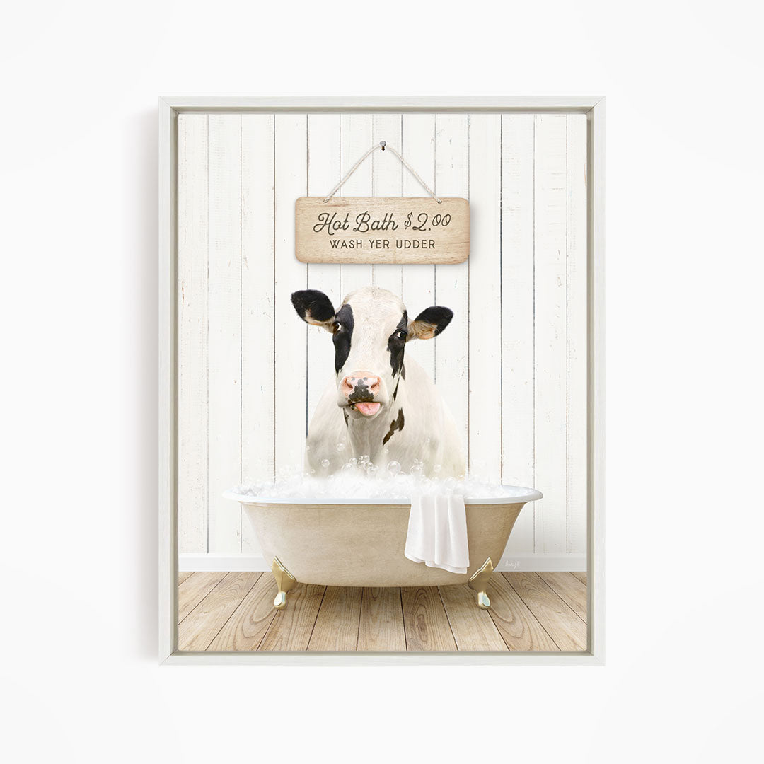 A black and white cow is sitting in a white bathtub, with a sign above it that reads "Hot Bath $2.00 WASH YER UDER".