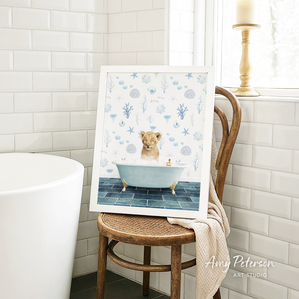 A framed print of a lion sitting in a bathtub is displayed on a wooden chair in a bathroom setting.