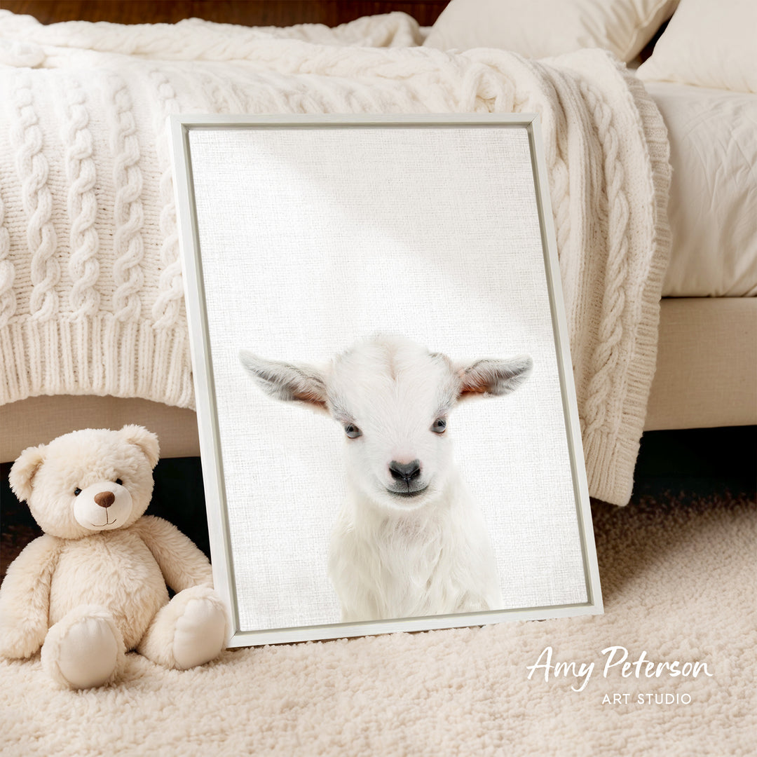 A framed image of a white lamb is displayed on a beige carpet, accompanied by a teddy bear.