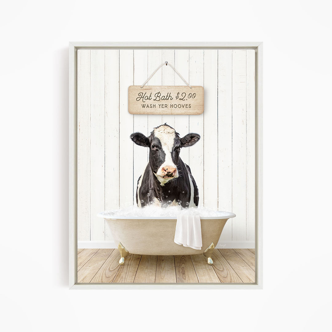 A black and white cow is sitting in a white bathtub, with a sign above it that reads "Hot Bath $2.00 WASH YER HOOVES".