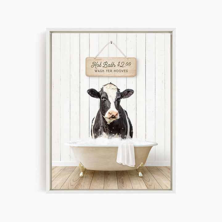 A black and white cow is sitting in a white bathtub, with a sign above it that reads "Hot Bath $2.00 WASH YER HOOVES".