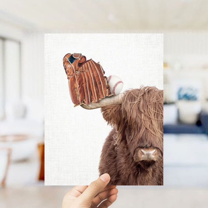 A hand holds up a collage of two images: a brown cow with a baseball glove on its head and a baseball in its mouth, and a blurred background of a living room.