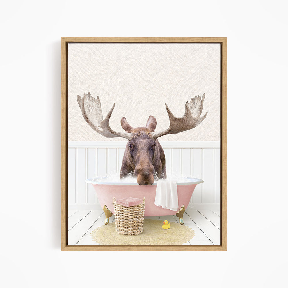 A moose is sitting in a pink bathtub filled with water, surrounded by a basket of rubber ducks and a towel.
