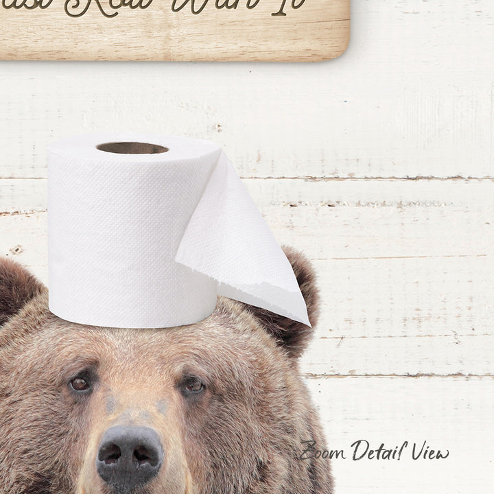 A brown bear wearing a roll of toilet paper on its head, with a wooden sign above it that says "Wanted".