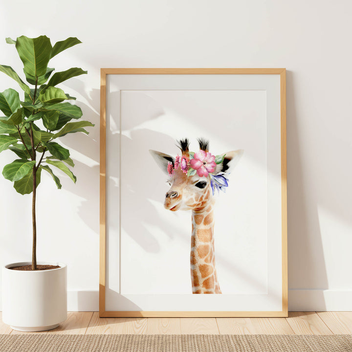 A framed print of a giraffe wearing a flower crown is displayed on a white wall, with a potted plant to the left.