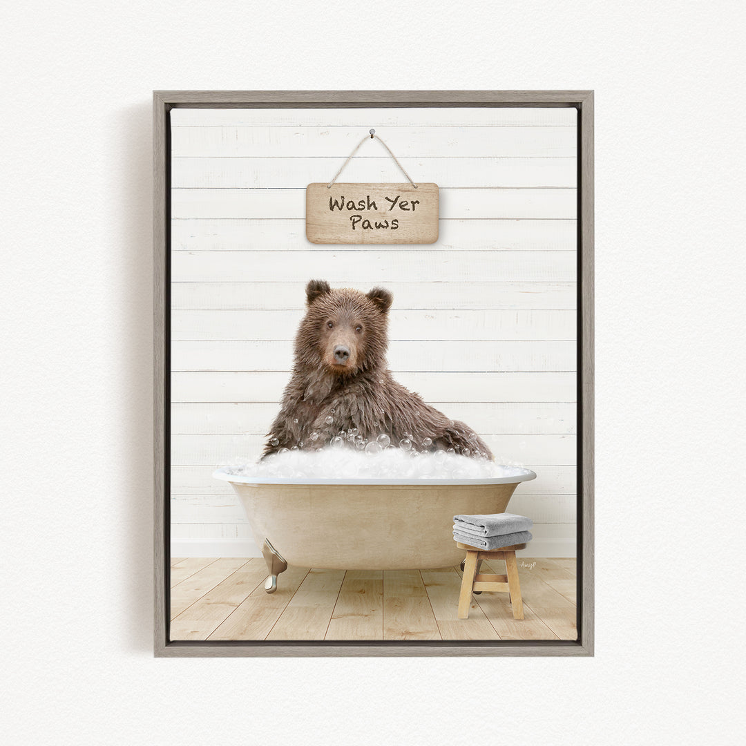 A brown bear sitting in a bathtub filled with bubbles, with a sign above that says "Wash Yer Paws".