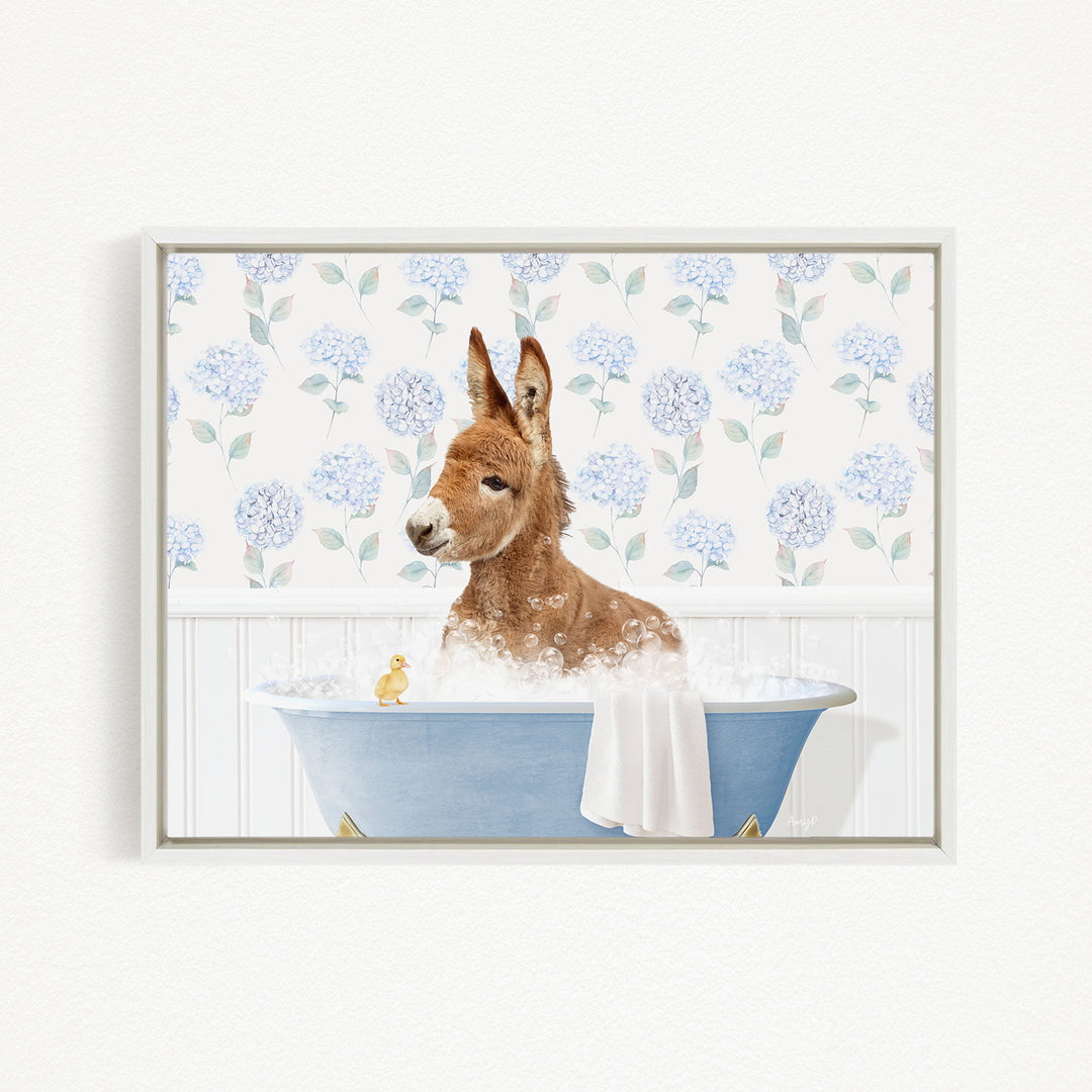 A brown donkey is sitting in a blue bathtub filled with bubbles, with a yellow duck floating on the water.