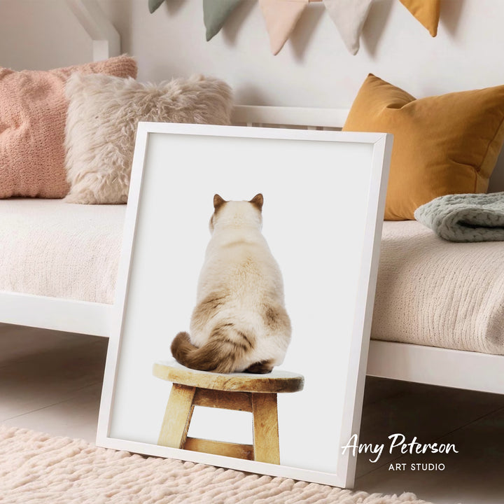A framed image of a cat sitting on a stool, with a cozy and inviting living room setting in the background.