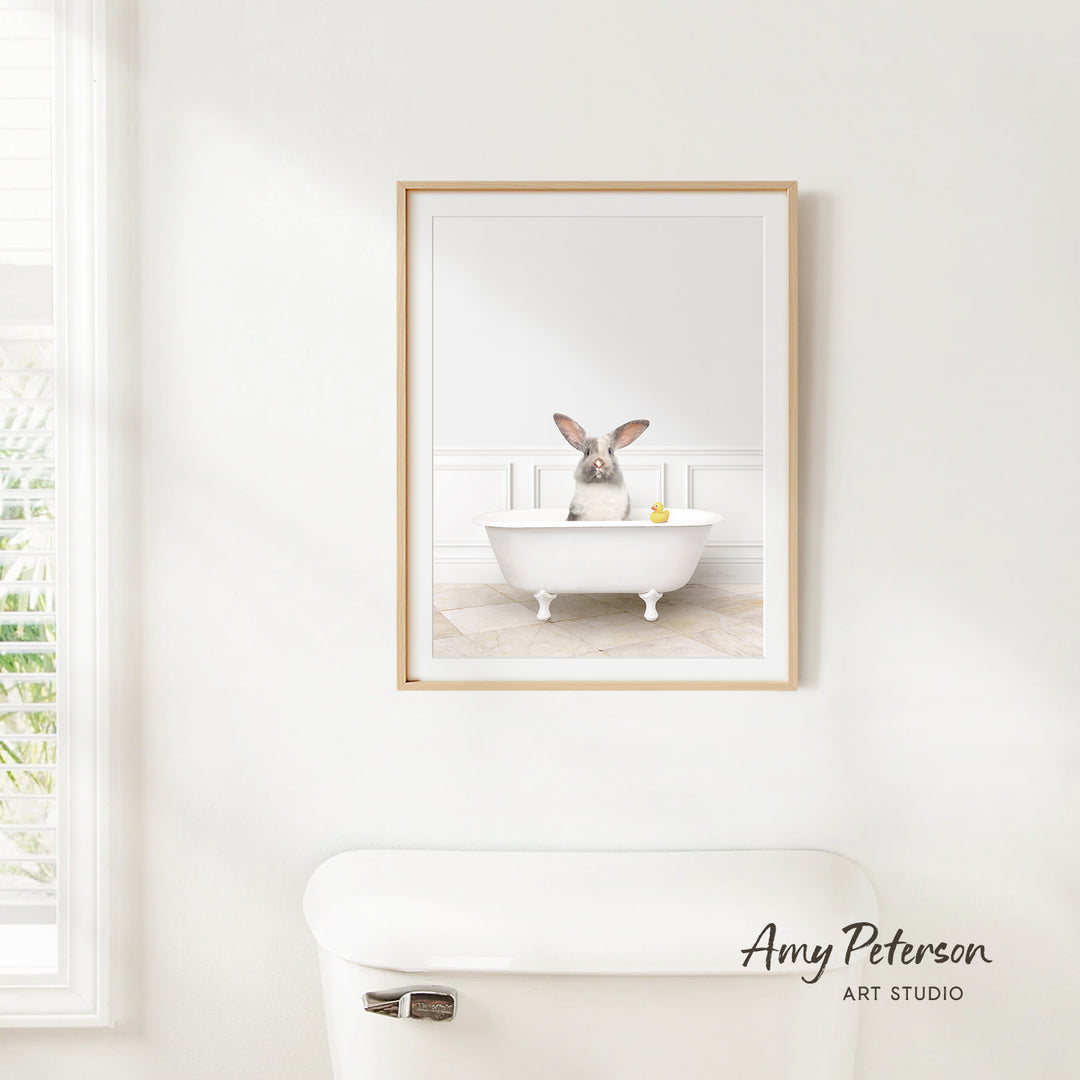 A framed image of a rabbit sitting in a white bathtub, with a yellow rubber duck floating in the water.