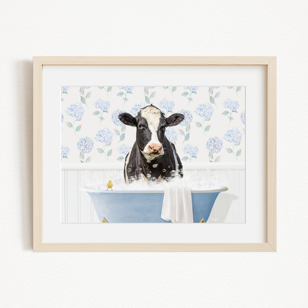A black and white cow is sitting in a blue bathtub filled with bubbles, with a white towel draped over the side of the tub.