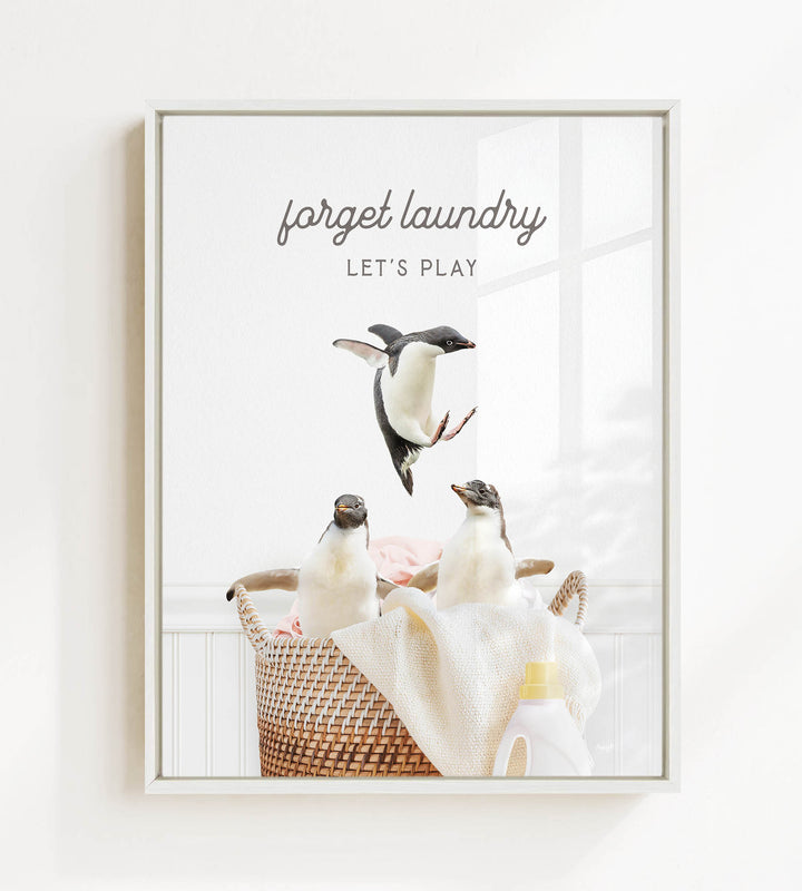 A framed image depicting three penguins in a laundry basket, with the text "forget laundry, let's play" written above them.