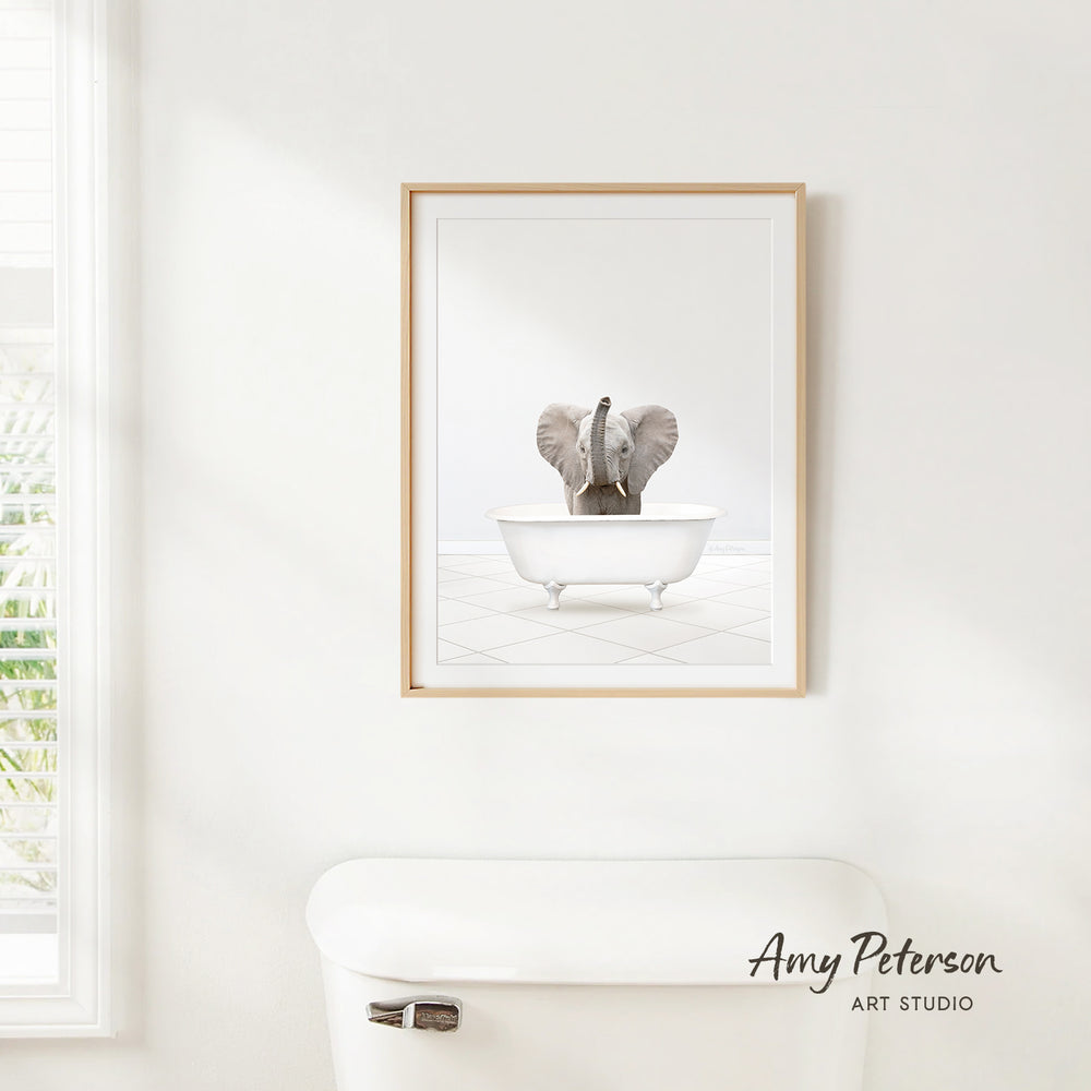 A framed image of an elephant sitting in a bathtub is hanging on a white wall.