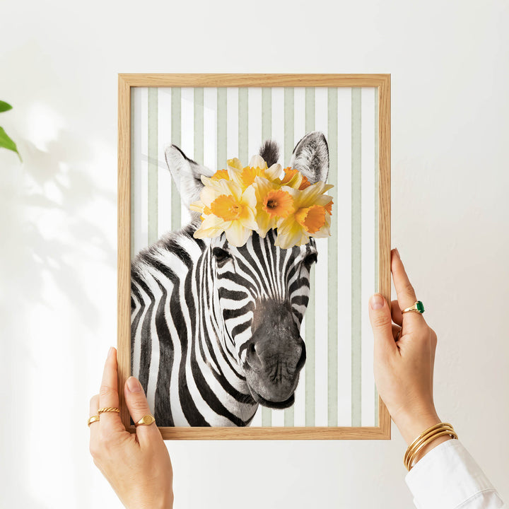 A person's hands are holding a framed picture of a zebra with a yellow flower crown on its head.