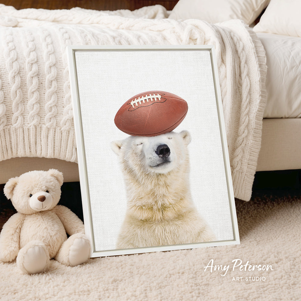 A framed image of a polar bear holding a football on its head, with a teddy bear sitting next to it on a bed.