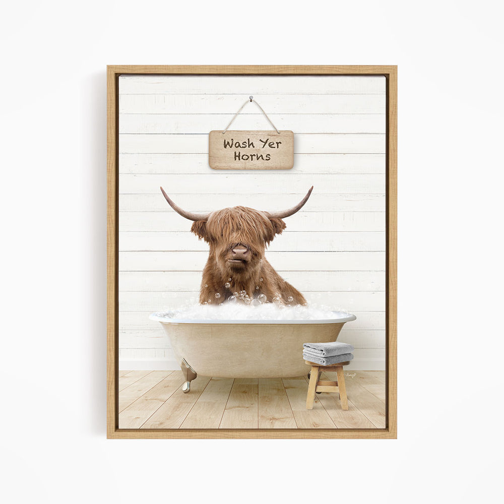 A brown Highland cow is sitting in a bathtub filled with water, with a sign above it that says "Wash Yer Horns".