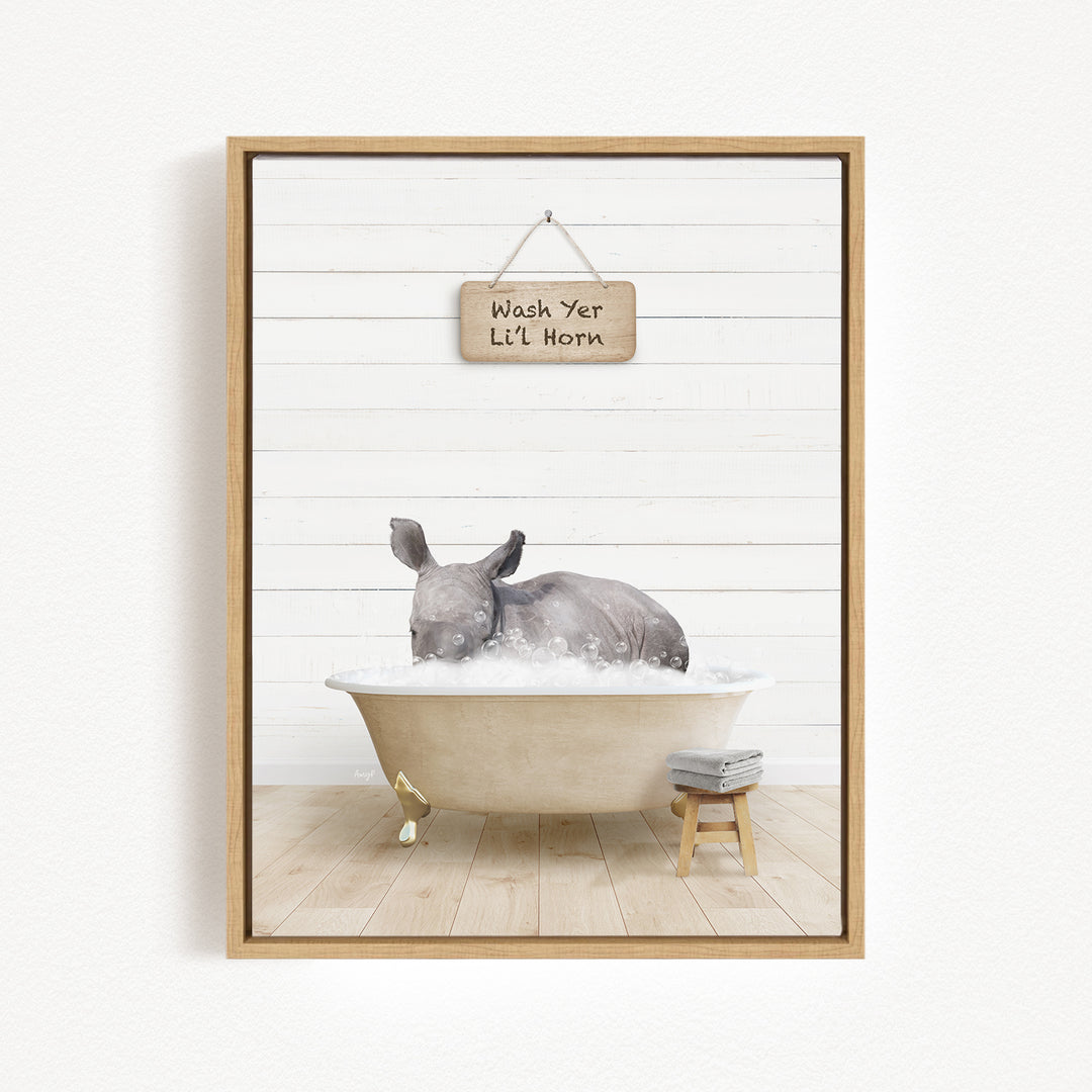 A rhinoceros is sitting in a bathtub filled with water, with a sign above it that says "Wash Yer Lil' Horn".