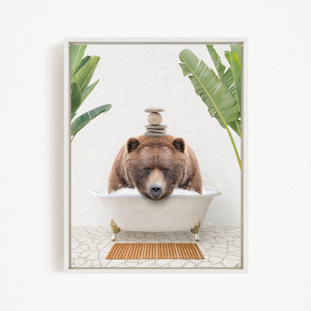 A brown bear is sitting in a white bathtub filled with water, surrounded by green leaves and a wooden mat on the floor.