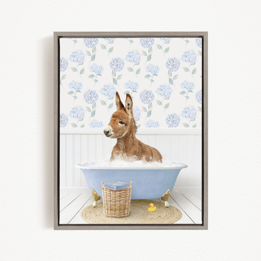 A donkey is sitting in a blue bathtub filled with bubbles, surrounded by a wicker basket and a rubber duck.