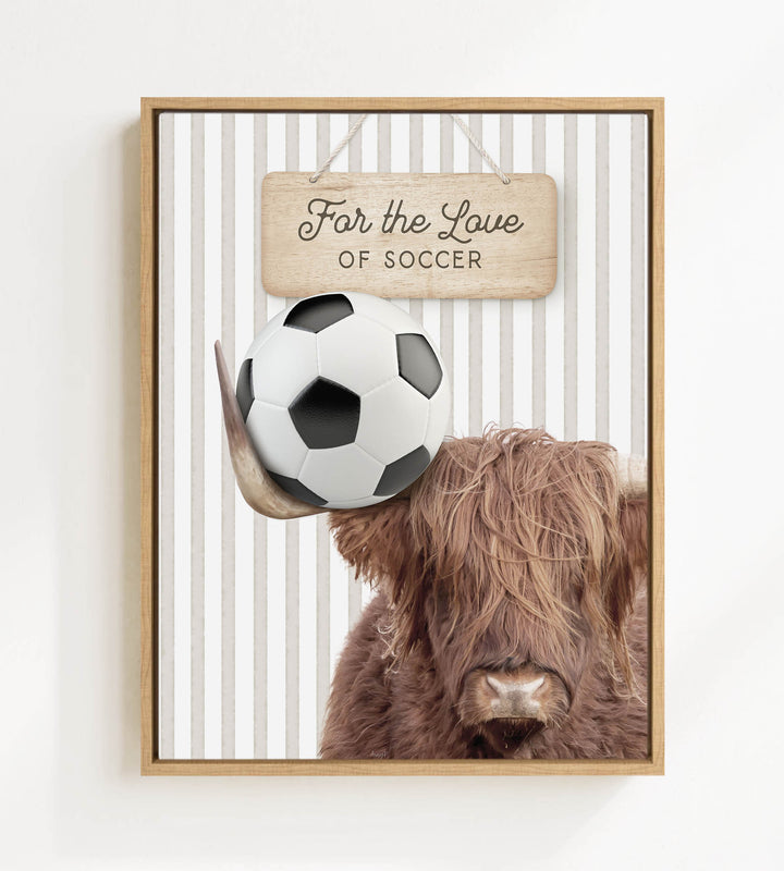 A framed image featuring a brown cow with a soccer ball on its head, with a wooden sign above that says "For the Love of Soccer".