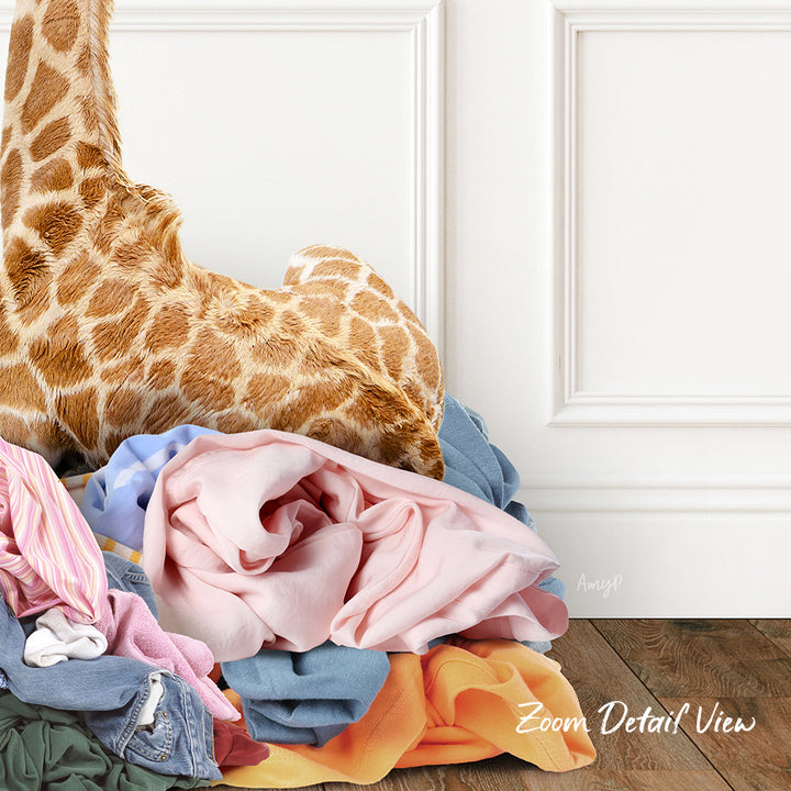 A pile of clothes, including a stuffed giraffe, is stacked on a wooden floor against a white wall.