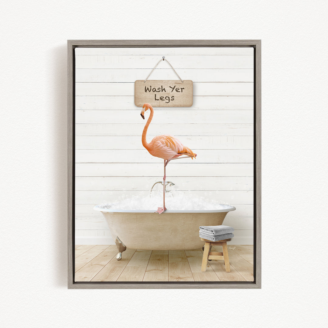 A framed image depicting a pink flamingo standing on one leg in a bathtub, with a sign above that reads "Wash Your Legs".
