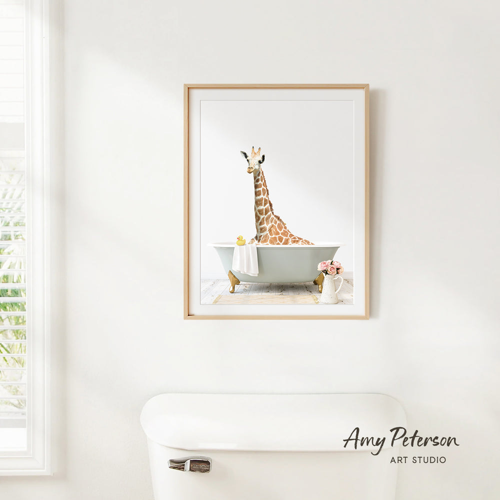 A framed print of a giraffe sitting in a bathtub is hanging on a white wall in a bathroom.