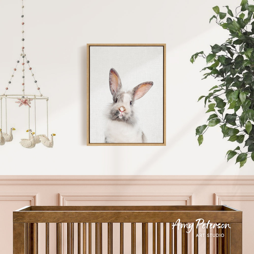 a wooden crib with a framed picture of a rabbit hanging on the wall above it.