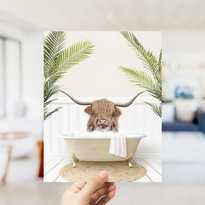 A hand holds up a framed image depicting a horned animal, likely a yak or a similar creature, sitting in a bathtub filled with water and surrounded by palm leaves.