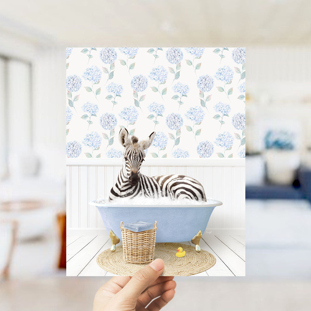 A zebra is sitting in a blue bathtub, surrounded by a wicker basket and a rubber duck, against a backdrop of a floral patterned wall.