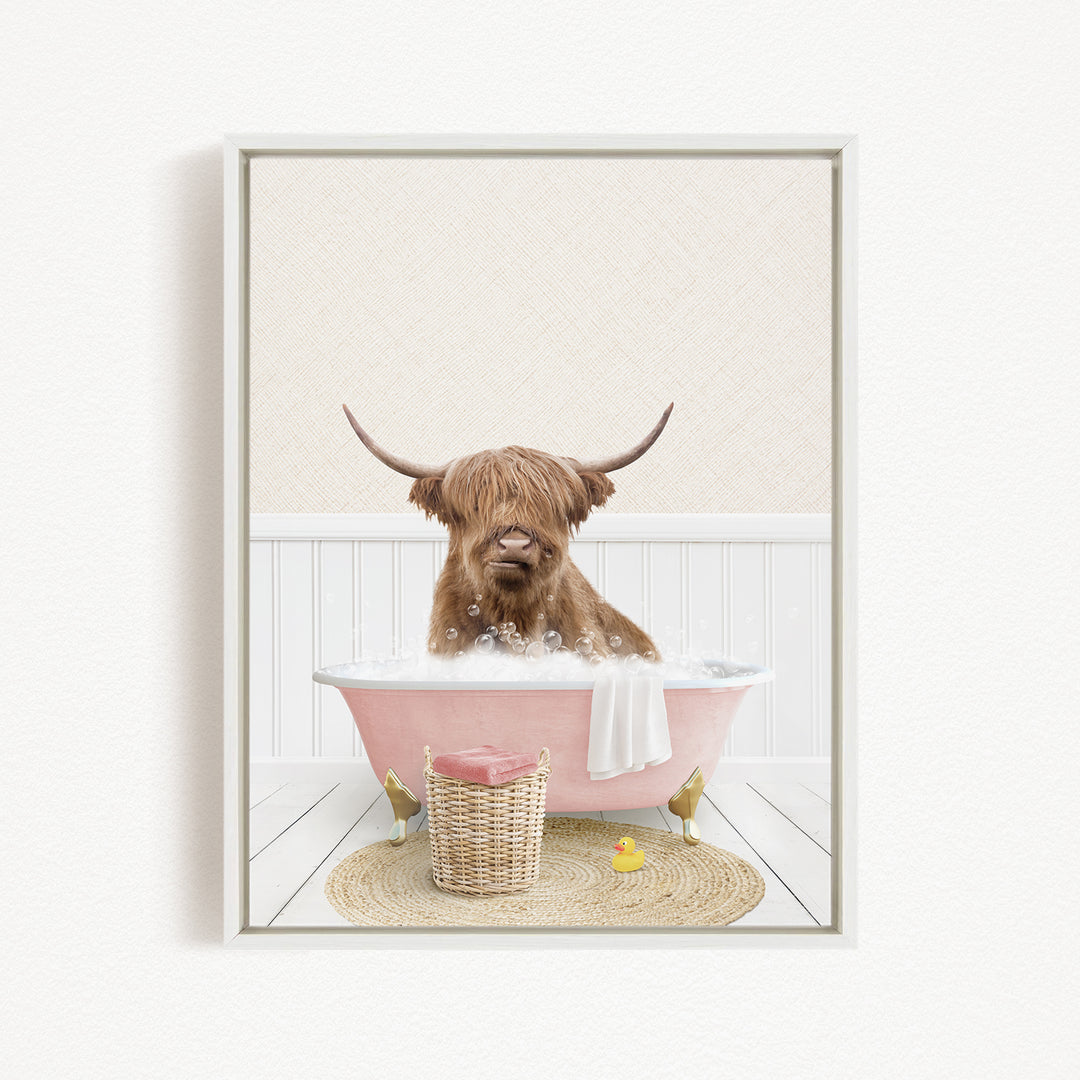 A Highland cow with long horns is sitting in a pink bathtub filled with bubbles, surrounded by a yellow rubber duck and a wicker basket.