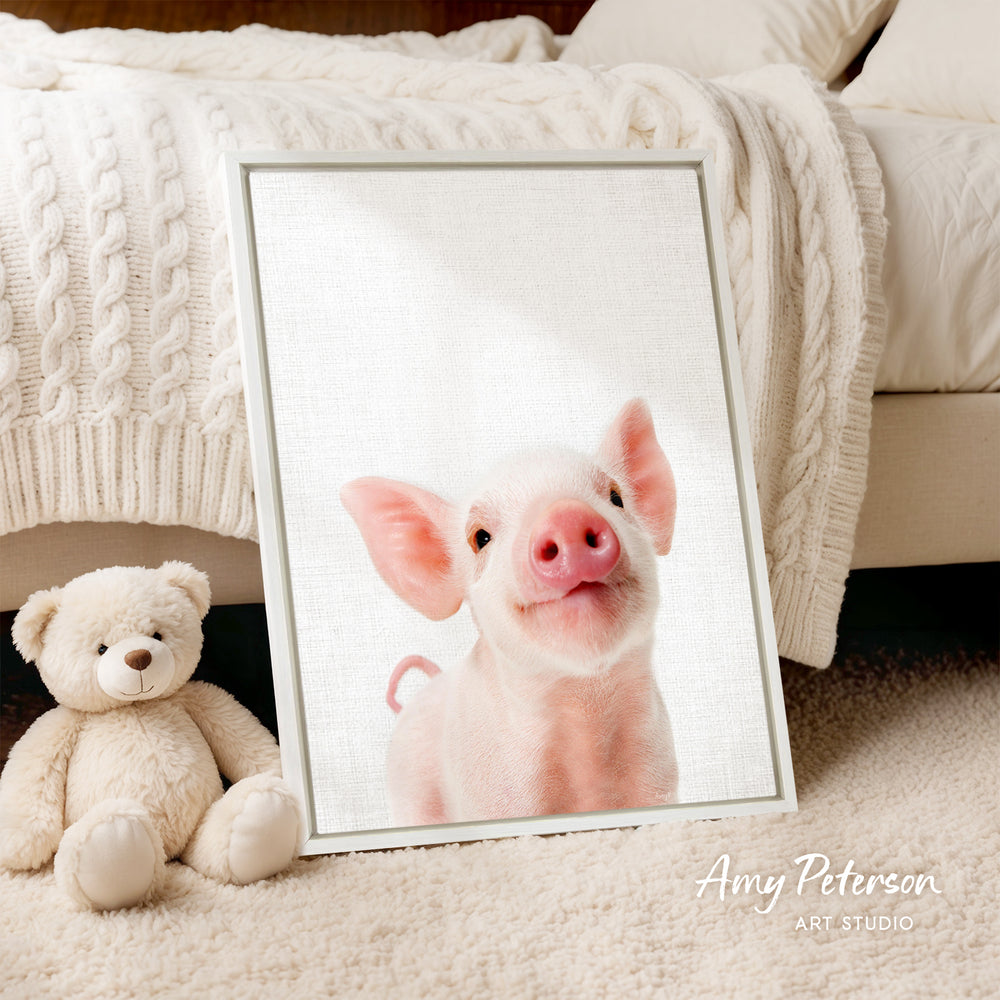 A framed image of a smiling pig is displayed on a white bedspread, accompanied by a teddy bear on the floor.
