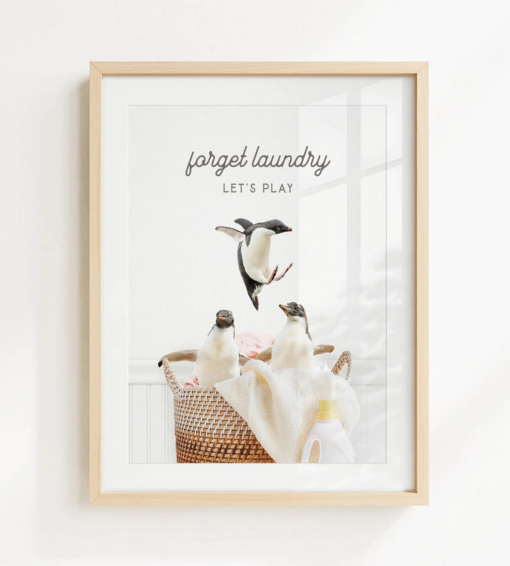 A framed image of three penguins in a basket, with the text "forget laundry, let's play" written above them.