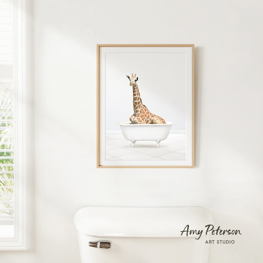 A framed print of a giraffe sitting in a bathtub is hanging on a white wall.