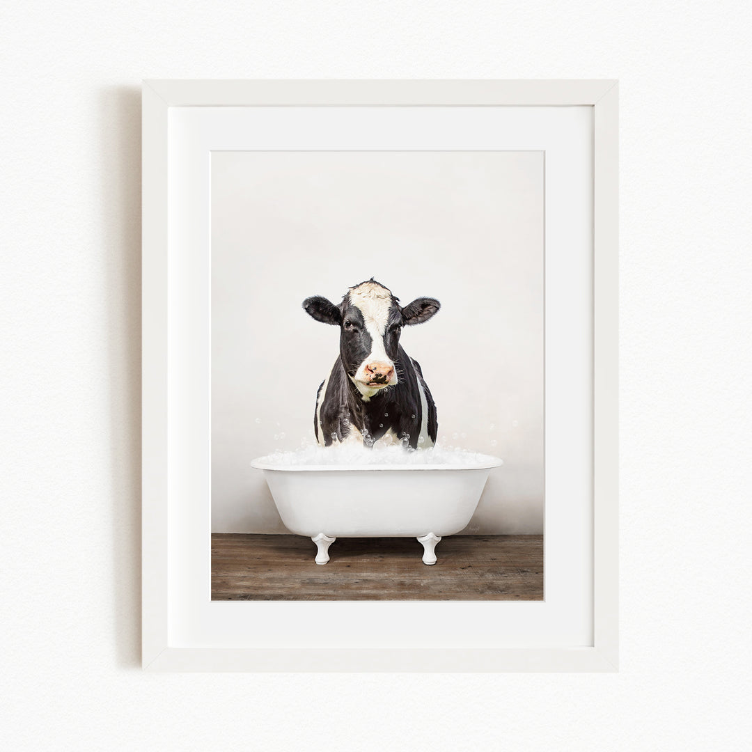 A black and white cow is sitting in a white bathtub filled with water, creating a whimsical and humorous scene.