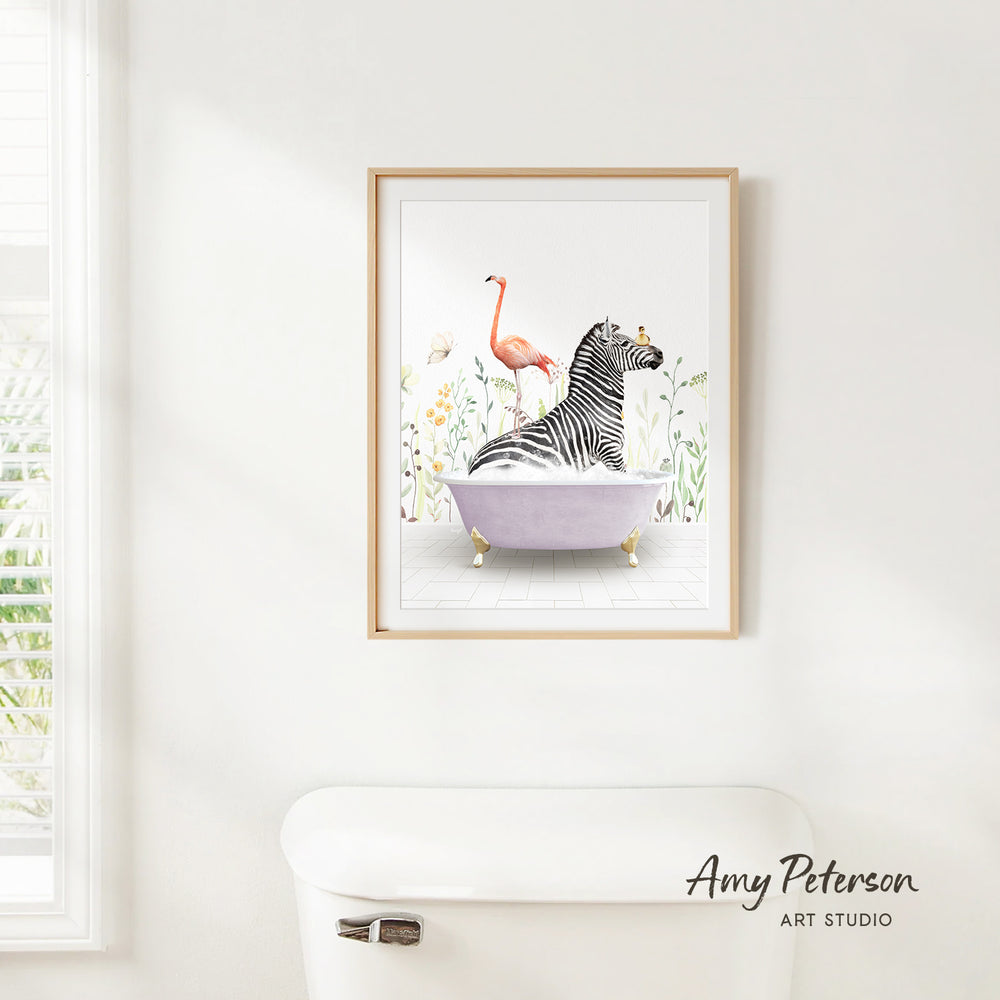 A framed illustration of a zebra sitting in a bathtub, surrounded by a pink flamingo and flowers, is hanging on a white wall.