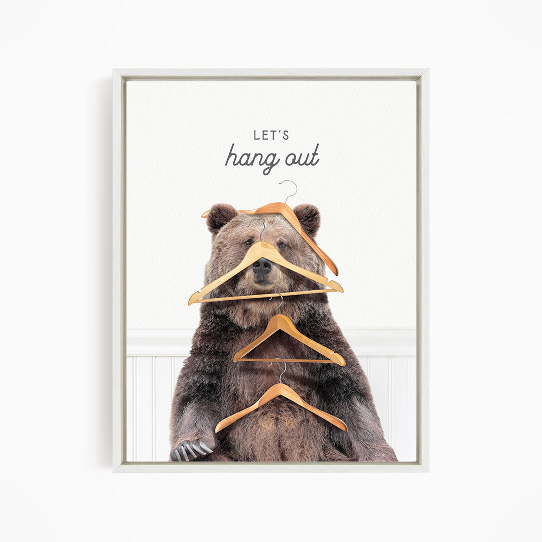 A brown bear sitting on a white surface, surrounded by hanging wooden hangers, with the text "Let's hang out" above it.