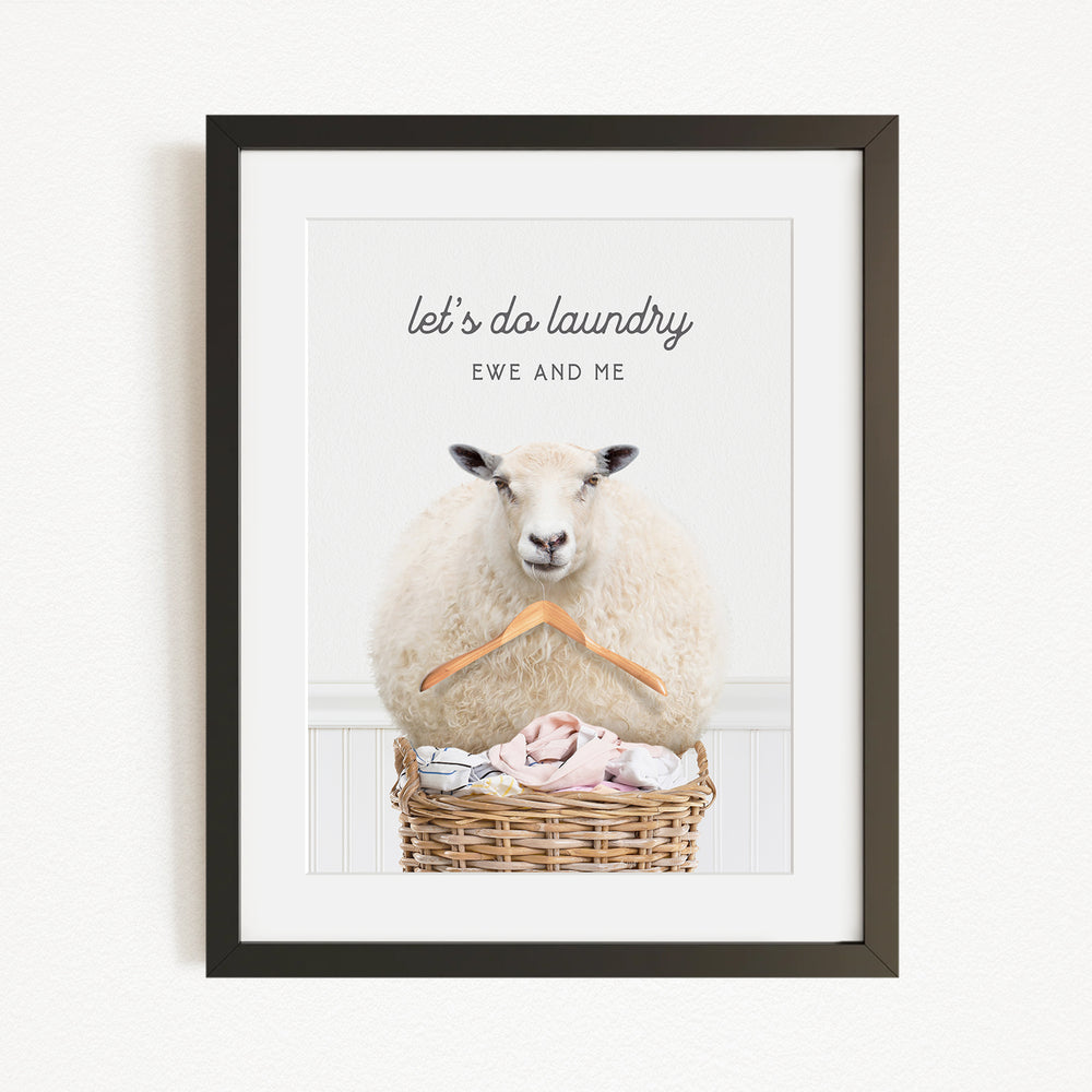A framed image of a sheep sitting in a wicker basket filled with laundry, with the text "let's do laundry EWE AND ME" displayed above the sheep.