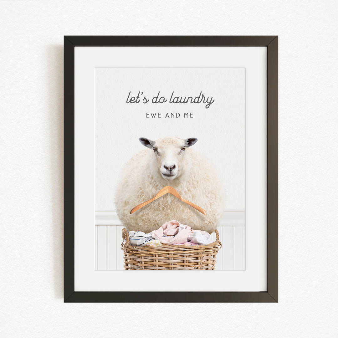 A framed image of a sheep sitting in a wicker basket filled with laundry, with the text "let's do laundry EWE AND ME" displayed above the sheep.