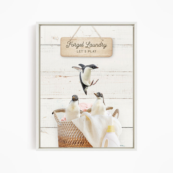 A framed image depicting three penguins in a basket, with a sign above that says "Forget Laundry, Let's Play".